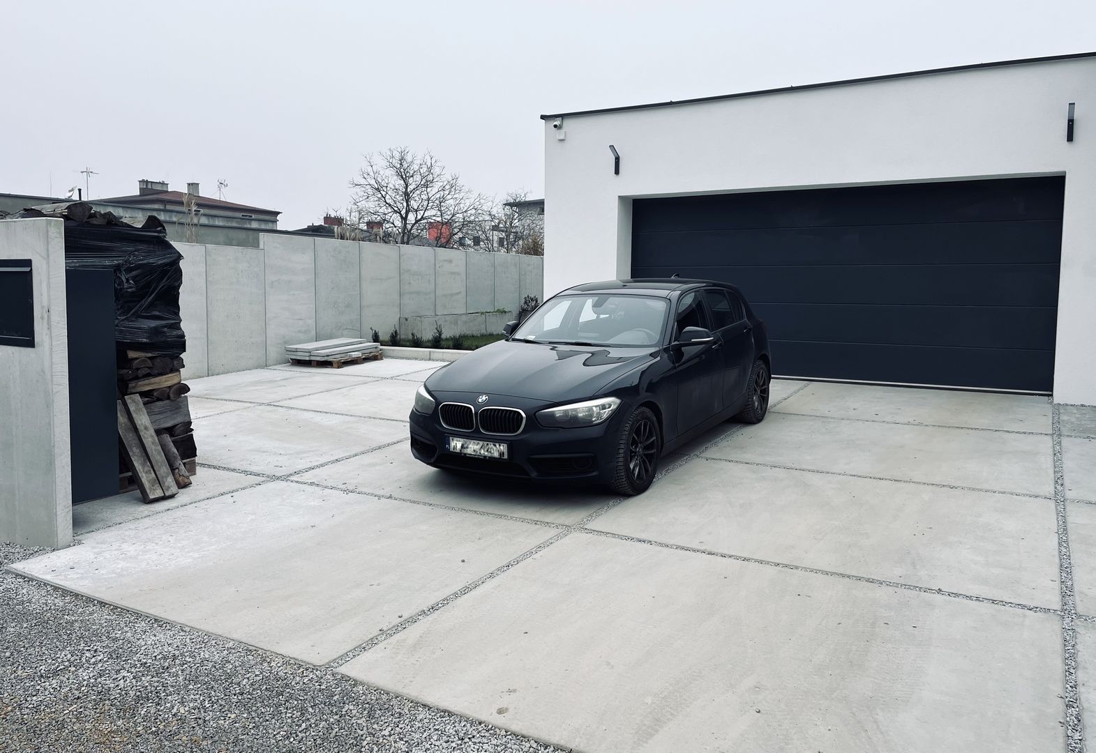 Fekete autó a betonfelhajtón. A háttérben egy garázs fekete bejárati kapuval.